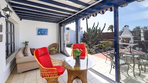 Une terrasse ensoleillée, dotée de chaises en osier, d’une table en verre et offrant une vue sur un jardin planté de cactus.