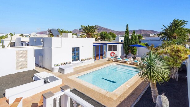 Une piscine sur le toit offrant une vue d égagée sur la mer et les montagnes, entourée de palmiers et bordée d’une architecture moderne.