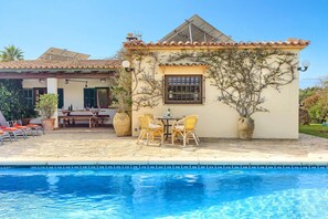 A poolside area with a dining table and chairs, a large potted plant, and a building with a tiled roof. - Villa Vinya Maria by Villa Plus (Mallorca)