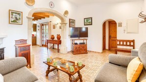 Una sala de estar con televisor, sofás, una mesa de centro y un comedor con una mesa dispuesta para el desayuno.