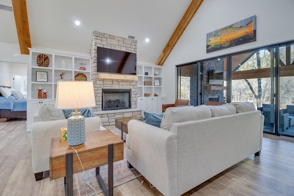 A modern living room with a stone fireplace, a large flat-screen TV, and a cozy sofa. - Waterfront Flippin Retreat w/ White River Access! (Flippin)