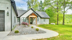 A modern house with a stone foundation, a wooden porch, and a well-maintained lawn. - Waterfront Flippin Retreat w/ White River Access! (Flippin)