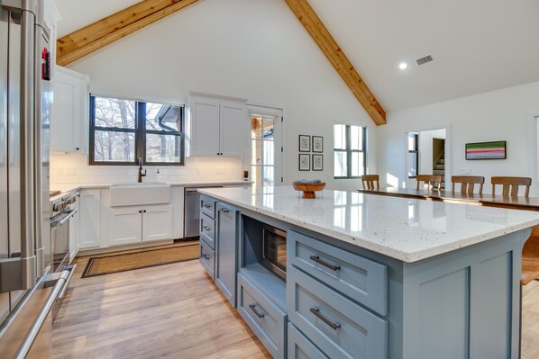 A modern kitchen with white cabinets, a large island, and wooden beams on the ceiling. - Waterfront Flippin Retreat w/ White River Access! (Flippin)