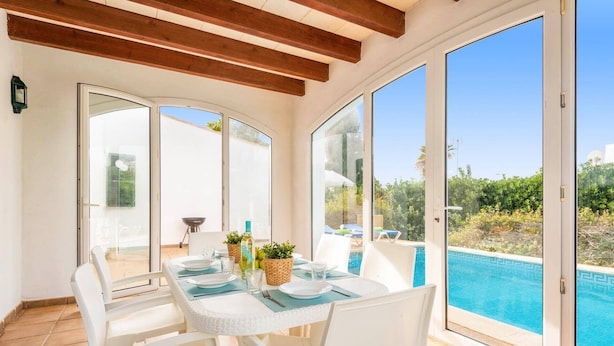 A dining area with a table set for two, overlooking a swimming pool. - Villa Bini Cinco by Villa Plus (Binibeca)