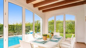A sunlit patio with a pool view, white furniture, and a table set for dining. - Villa Bini Cinco by Villa Plus (Binibeca)