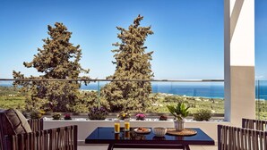 Un balcone con un tavolo apparecchiato per la colazione, affacciato su un paesaggio costiero con alberi e il mare.