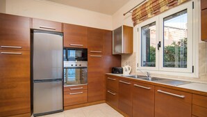 A modern kitchen with wooden cabinets, a stainless steel refrigerator, an oven, a toaster, and a window with a view of greenery.