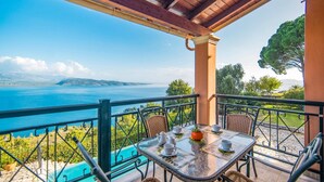A terrace with a table set for dining, overlooking a scenic view of the sea and hills.