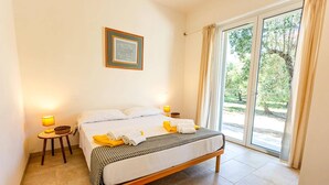 Ein ordentlich bezogenes Bett mit einer karierten Tagesdecke, zwei Kissen und einem gefalteten Handtuch auf einem hölzernen Bettgestell. Zwei Nachttischlampen und ein gerahmtes Zertifikat sind an der Wand zu sehen.
