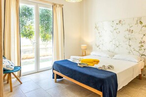 Ein Hotelzimmer mit Bett, Sessel, Lampe und Blick auf Grünflächen.