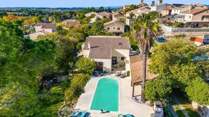 Vista aerea di una zona residenziale con piscina circondata da sedie a sdraio, una chiesa e vista sul paesaggio circostante.