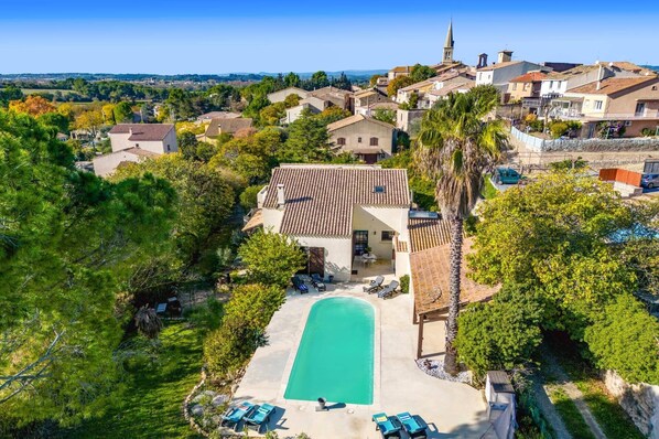 An aerial view of a residential area with a swimming pool surrounded by lounge chairs, a church, and a view of the distant landscape.