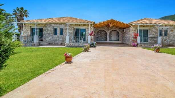 Une maison en pierre à deux étages, avec un toit en tuiles, une entrée centrale surmontée d’un arc et une allée pavée.