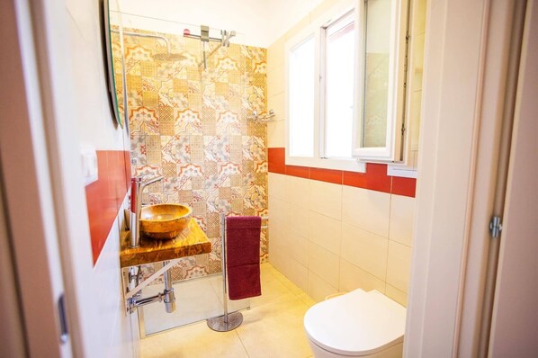 Une petite salle de bain avec une douche, un lavabo en bois, une serviette rouge et des toilettes blanches.