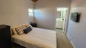 Een slaapkamer met een bed, nachtkastje, televisie en een deur naar een badkamer.