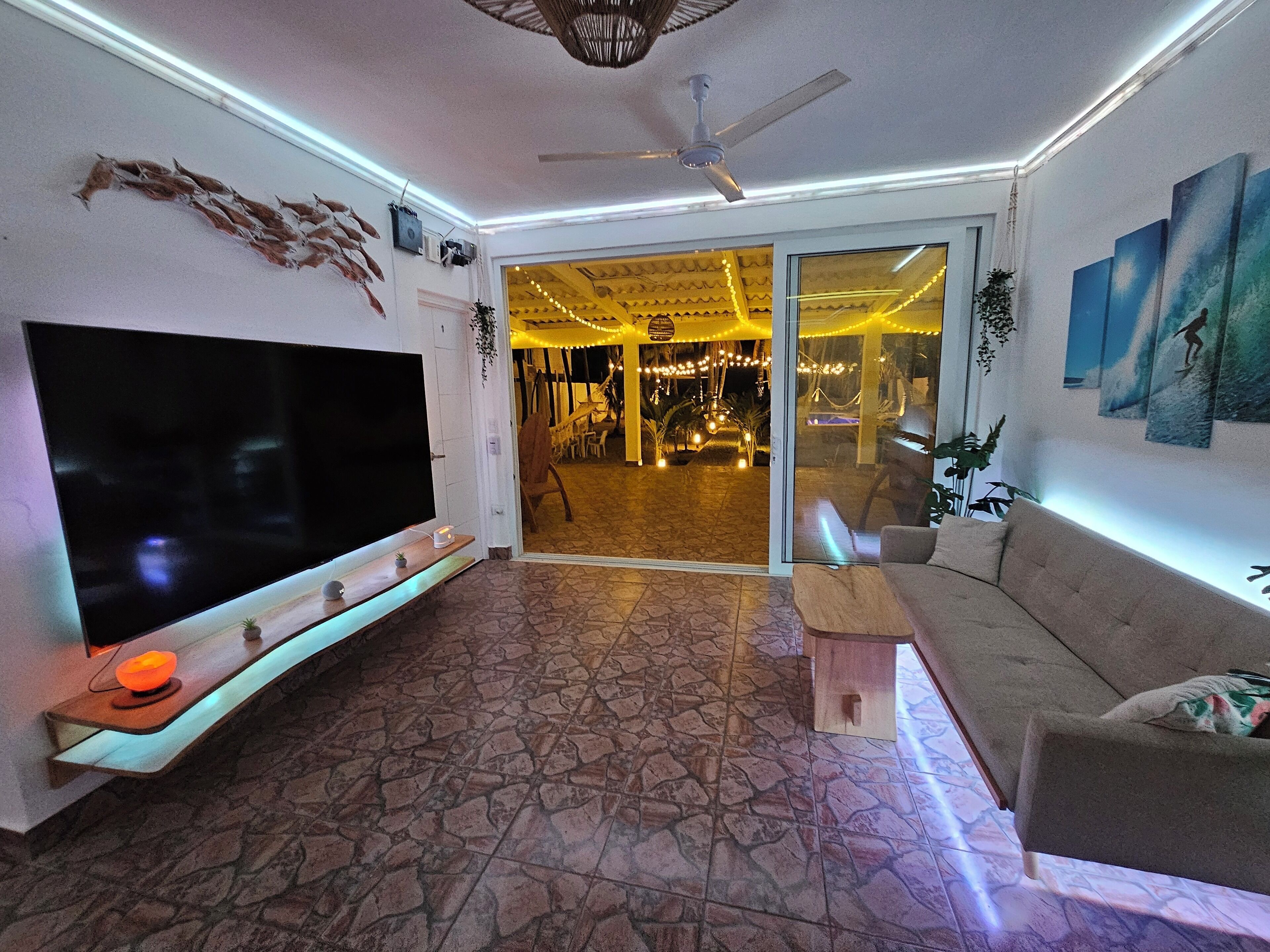 A living room with a flat-screen TV, a ceiling fan, and a stone-patterned floor.