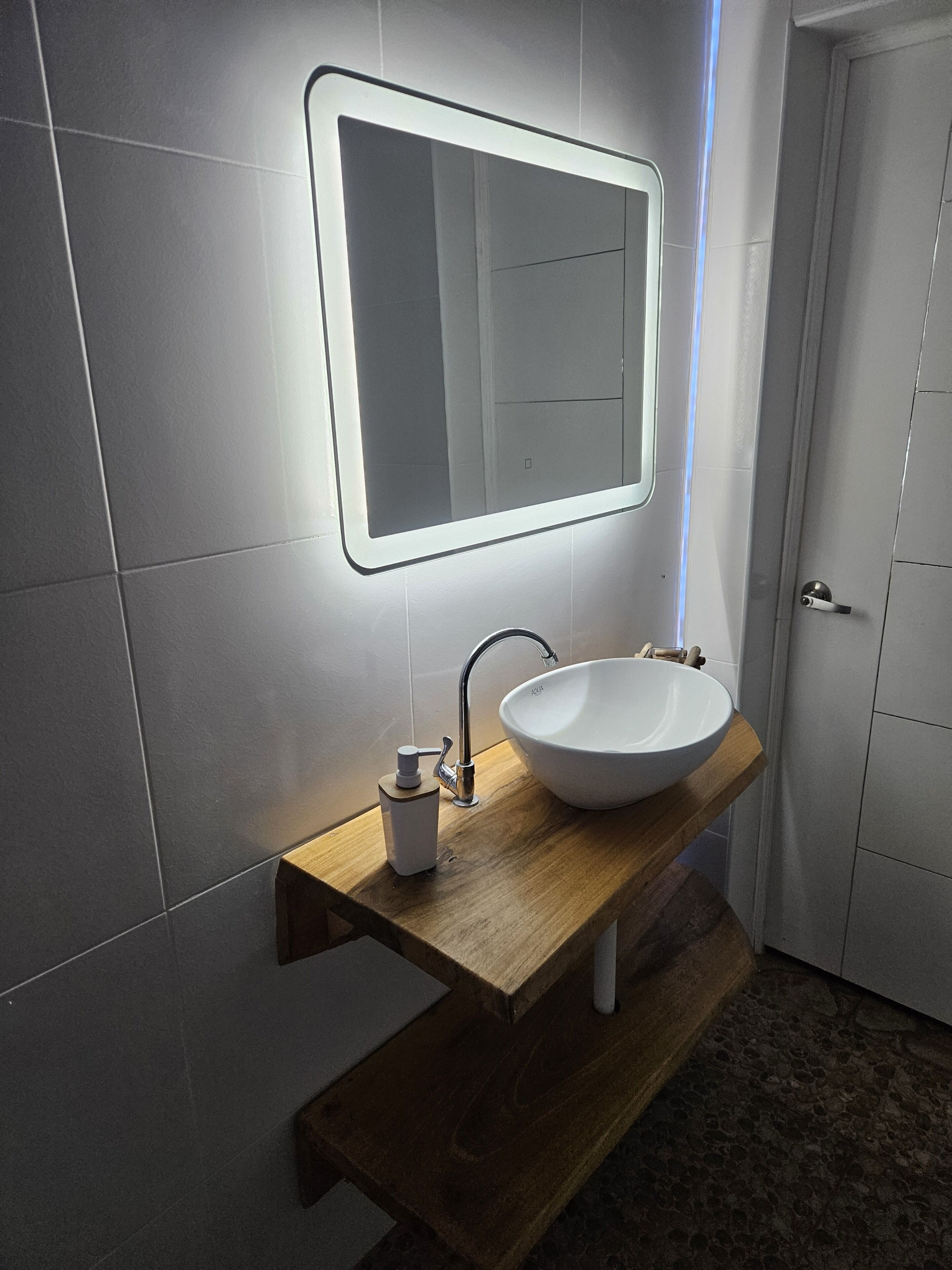 Un baño con lavamanos blanco, espejo y tocador de madera.