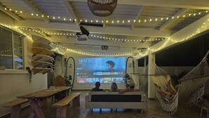 Una habitación acogedora con una pantalla grande mostrando una película, muebles de madera y luces de estilo guirnalda.
