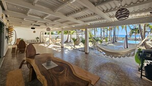 Un espacio interior amplio con una mesa de madera, hamacas y vista a la playa.