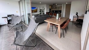 Een moderne woonruimte met een eethoek, een bank, een keuken en een glazen schuifdeur naar een balkon.
