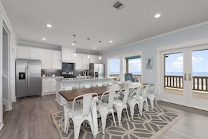 A modern kitchen with white cabinetry, a central island, and a dining area with white chairs.