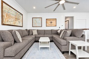 A modern living room with a sectional sofa, a coffee table, and a rug. There are two framed maps on the wall.