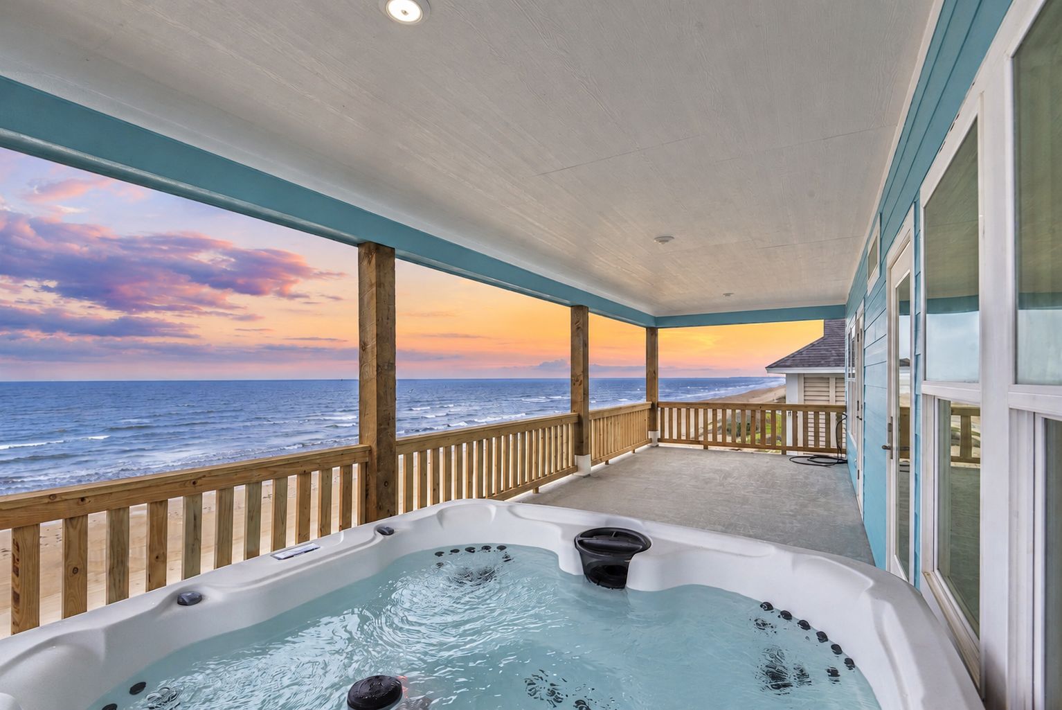 A covered outdoor area with a hot tub, wooden deck, and a view of the ocean.