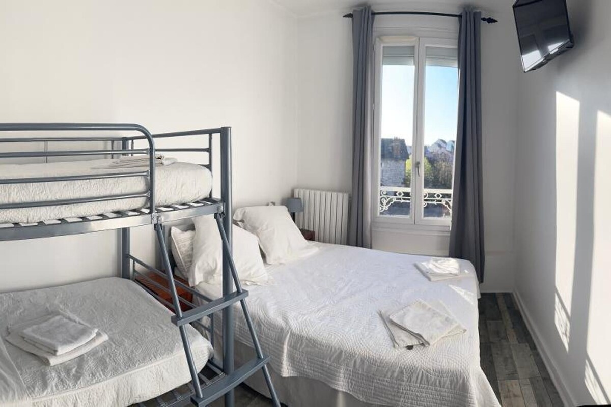 Une chambre avec des lits superposés, une lampe de chevet, une fenêtre avec des rideaux et une vue sur l’extérieur.