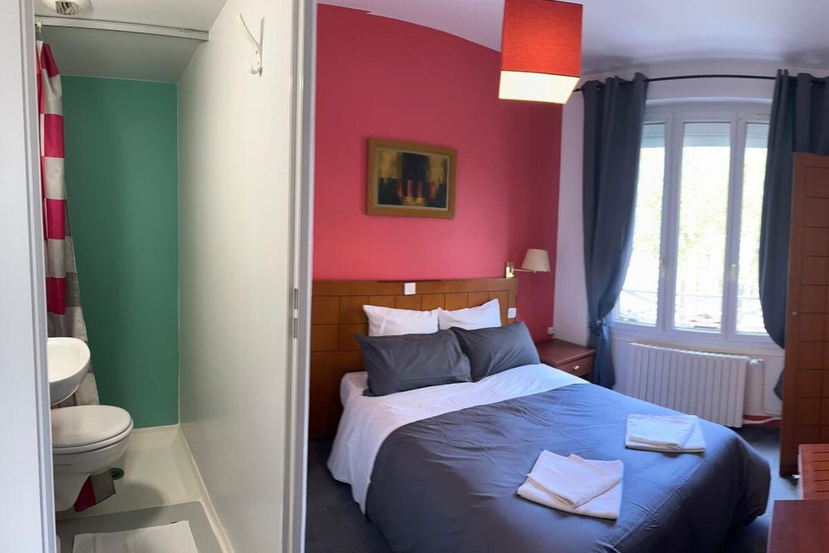A hotel room with a bed, a window with curtains, a radiator, and a door.