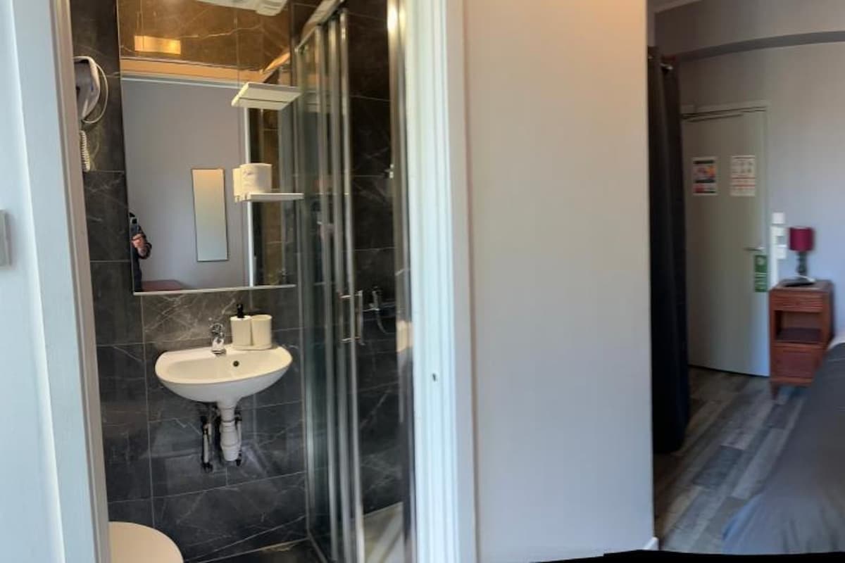 A hotel room with a bed, a bedside table, a mirror, and a bathroom with a sink and shower.