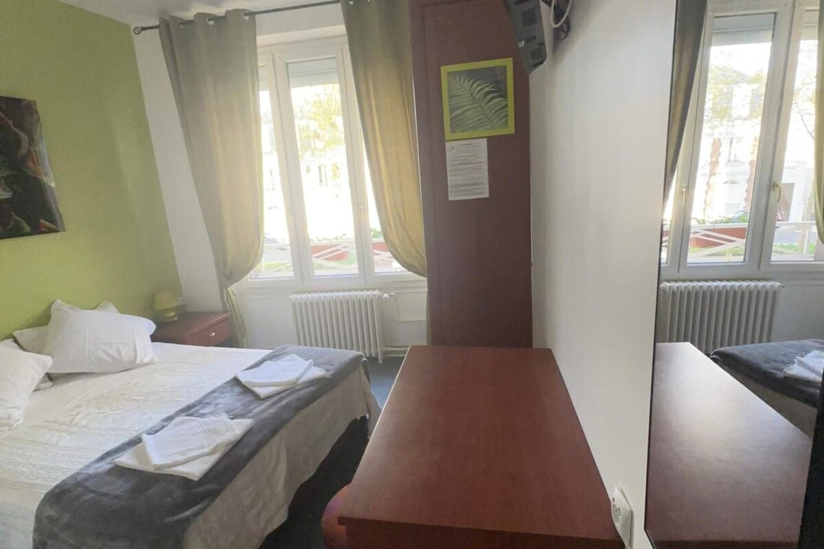 Een hotelkamer met een bed, een houten bureau, een wandtelevisie en een raam met gordijnen.