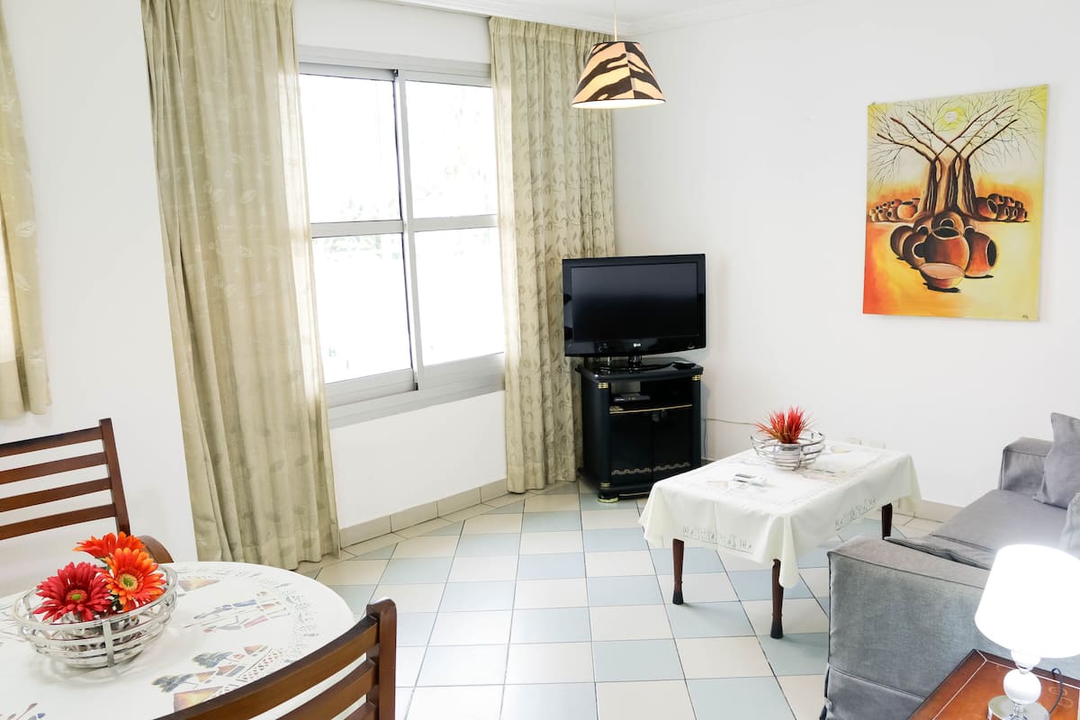 Una sala de estar con una mesa de comedor, sillas, un sofá, un televisor y un cuadro en la pared.