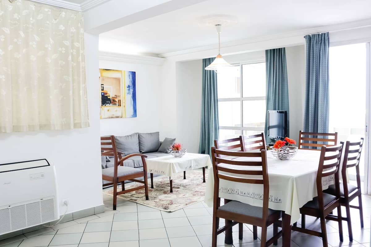 Un comedor con una mesa dispuesta para cuatro personas, un sofá y un televisor al fondo.