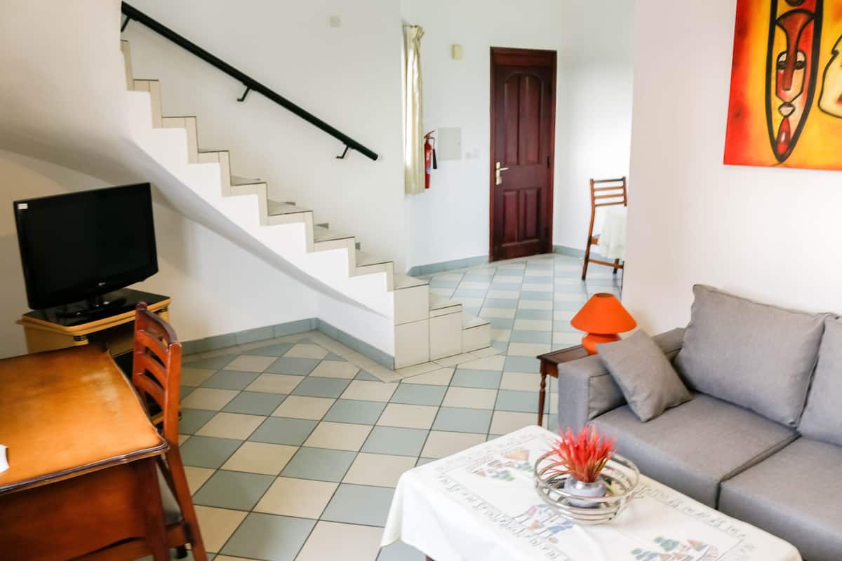 Una sala de estar con sofá, mesa de centro, televisor, escalera y puerta.
