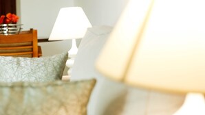 Een detail van een bed met een gekleurd kussen en een witte lamp op de achtergrond.
