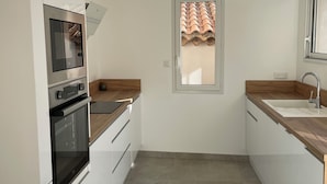 A modern kitchen with white cabinets, a built-in oven, a microwave, and a wooden countertop. - L'écurie - New house for 5 people, swimming pool (Portiragnes)