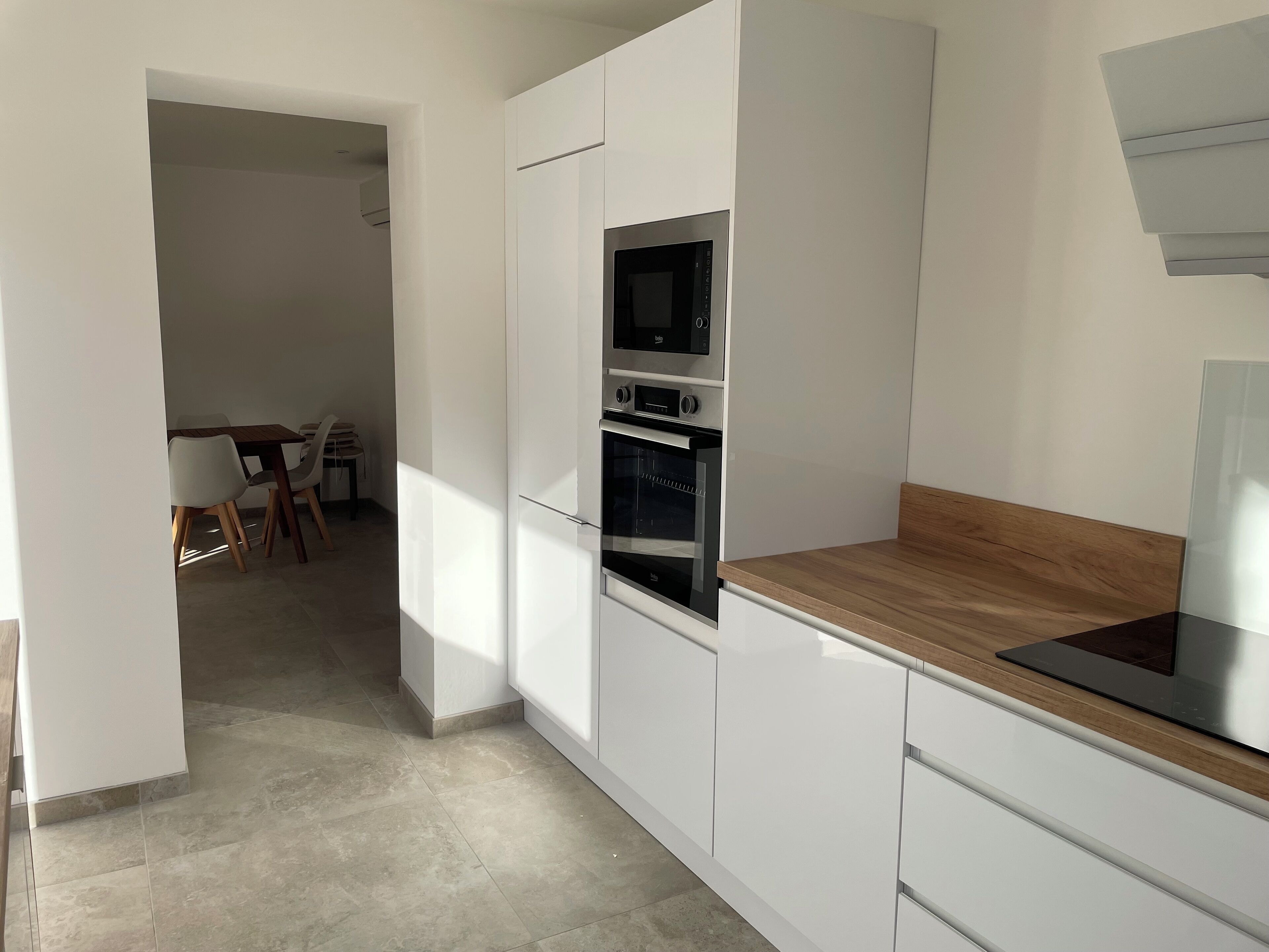 Een moderne keuken met witte kasten, een houten aanrechtblad en geïntegreerde apparatuur, waaronder een magnetron en oven.