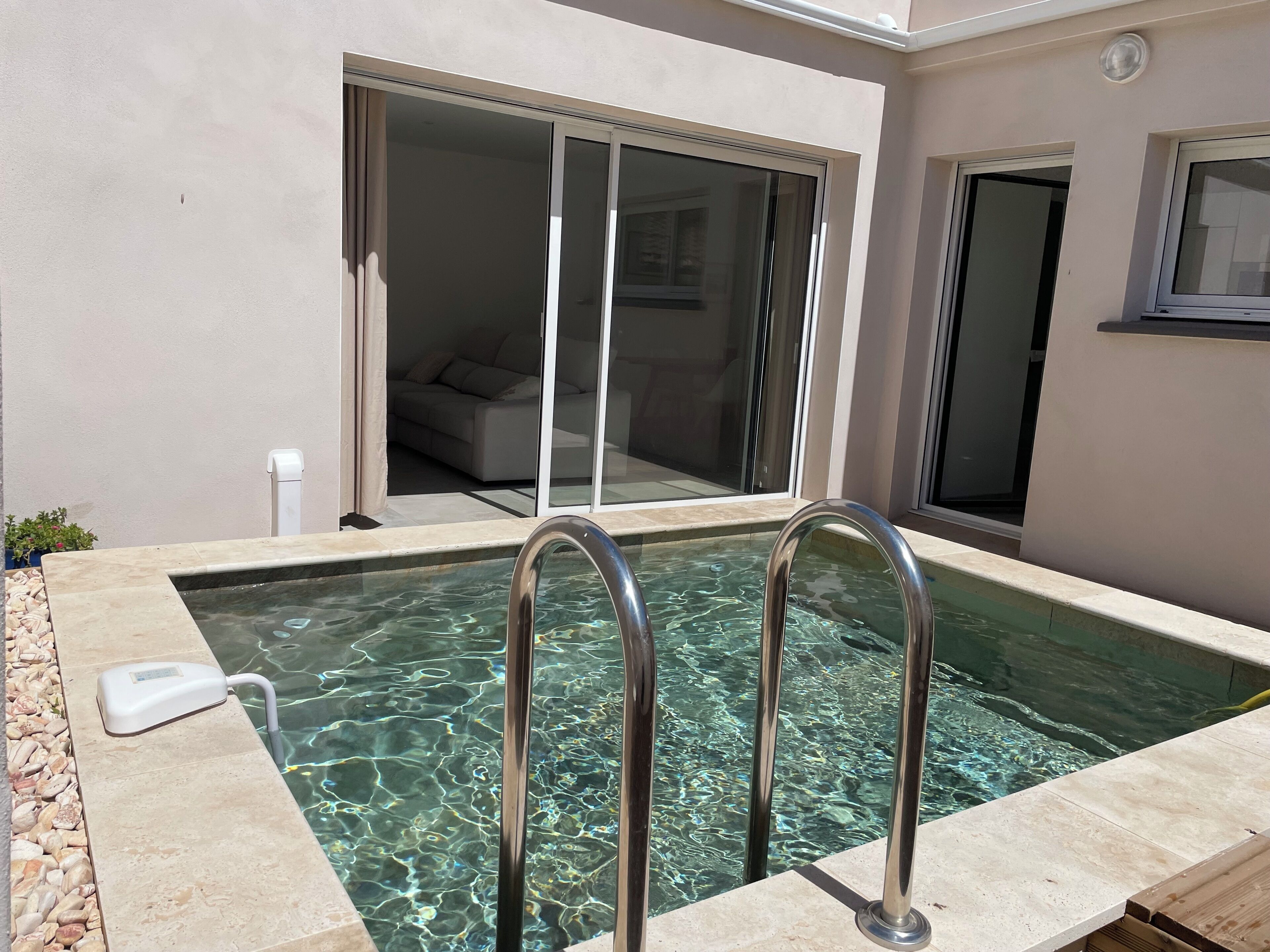 A swimming pool with metal ladders, a white exterior wall, and a sliding glass door leading to a living area.