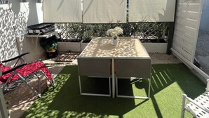 A patio area with a table and chairs, surrounded by artificial grass and a decorative ceiling.