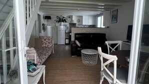 A spacious living area with a sofa, coffee table, and a dining table with chairs. A kitchen with a stove and cabinets is visible in the background.