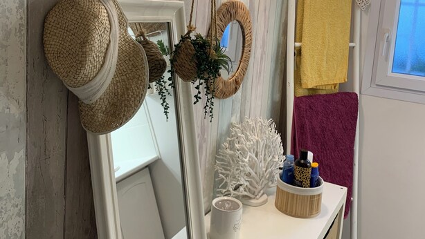 A bathroom with a white vanity, a mirror, a shelf with toiletries, and a window.