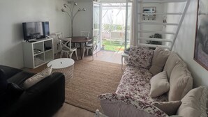A living room with a sofa, a TV, a dining table with chairs, and a staircase leading to a balcony.