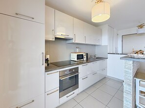 Een moderne keuken met witte kasten, een magnetron, een oven en een spoelbak.