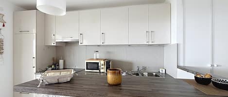 A kitchen with white cabinets, a wooden countertop, a microwave, and a hanging light fixture.