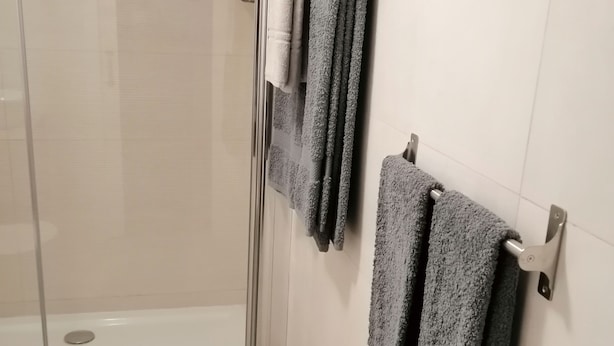 A bathroom with a glass shower door, white tiled walls, and two towels hanging on a towel rack. - VILLA FRESCURA DO MAR EM SETUBAL (Setubal)