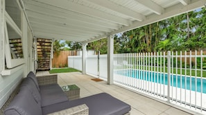 A covered patio area with a pool, a white fence, and a wooden deck.