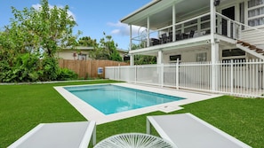 A backyard with a swimming pool, a covered patio, and a fenced area.
