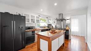 A modern kitchen with a black refrigerator, wooden island, stainless steel appliances, and white cabinetry.
