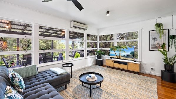 A spacious living room with large windows, a comfortable sofa, a coffee table, and a view of a tropical landscape.