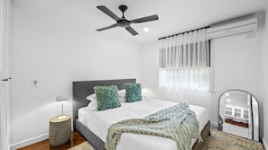 A bedroom with a bed, a ceiling fan, a bedside lamp, a window with curtains, and a mirror.